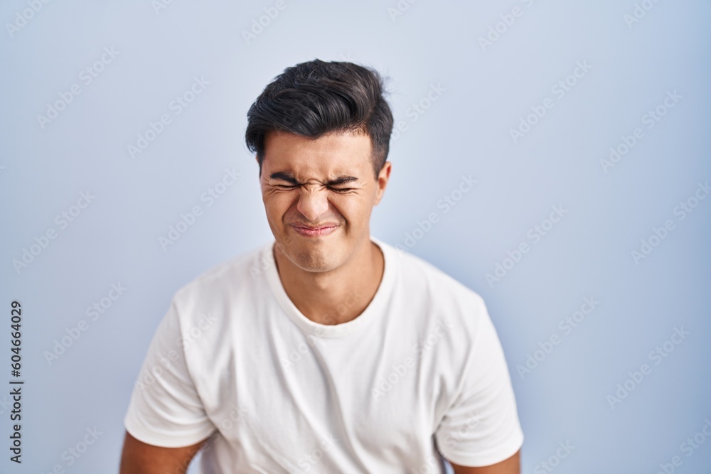 Hispanic man standing over blue background with hand on stomach because indigestion, painful illness feeling unwell. ache concept. Hispanic man standing over blue background with hand on stomach because indigestion, painful illness feeling unwell. ache concept.