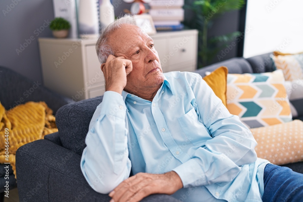 Fototapeta premium Middle age grey-haired man sitting on sofa with serious expression at home