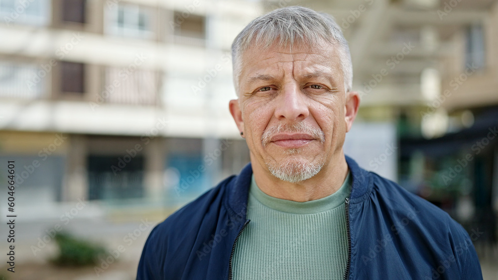 Middle age grey-haired man standing with serious expression at street Middle age grey-haired man standing with serious expression at street