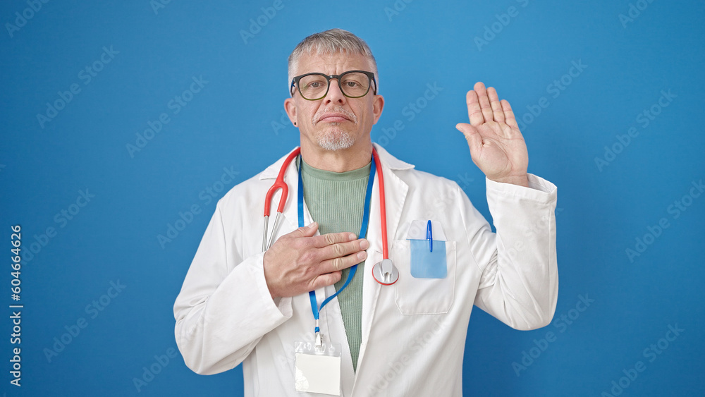 Middle age grey-haired man doctor making an oath with hand on chest over isolated blue background Middle age grey-haired man doctor making an oath with hand on chest over isolated blue background