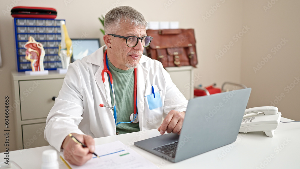 Middle age grey-haired man doctor using laptop working at clinic Middle age grey-haired man doctor using laptop working at clinic