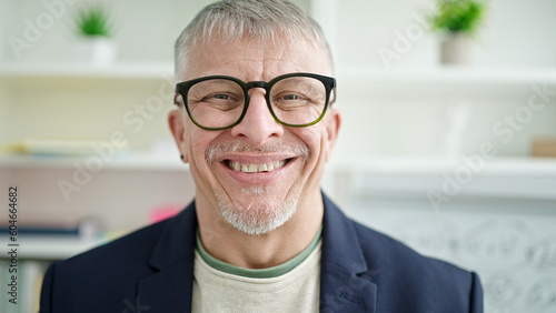 Middle age grey-haired man teacher smiling confident standing at university classroom