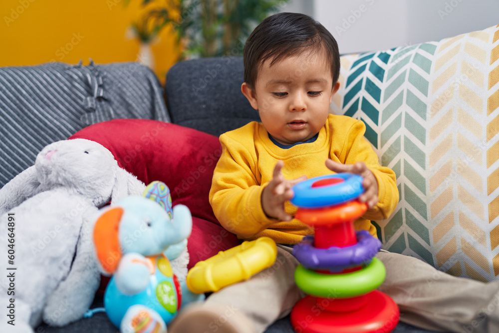 Adorable hispanic boy playing with hoops game sitting on sofa at home Adorable hispanic boy playing with hoops game sitting on sofa at home