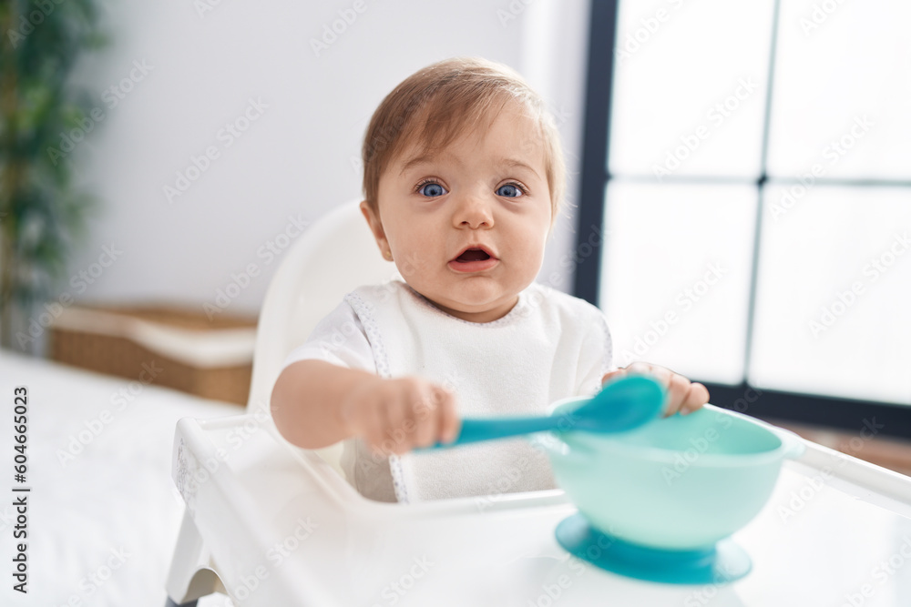 Adorable caucasian baby sitting on highchair holding spoon at bedroom Adorable caucasian baby sitting on highchair holding spoon at bedroom