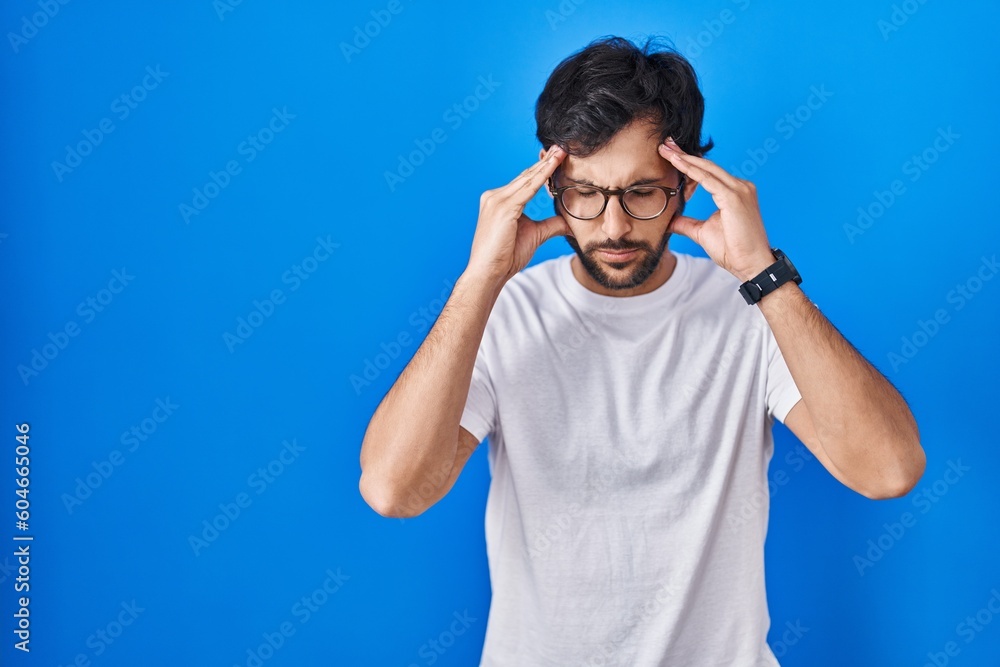 Fototapeta premium Handsome latin man standing over blue background with hand on head for pain in head because stress. suffering migraine.