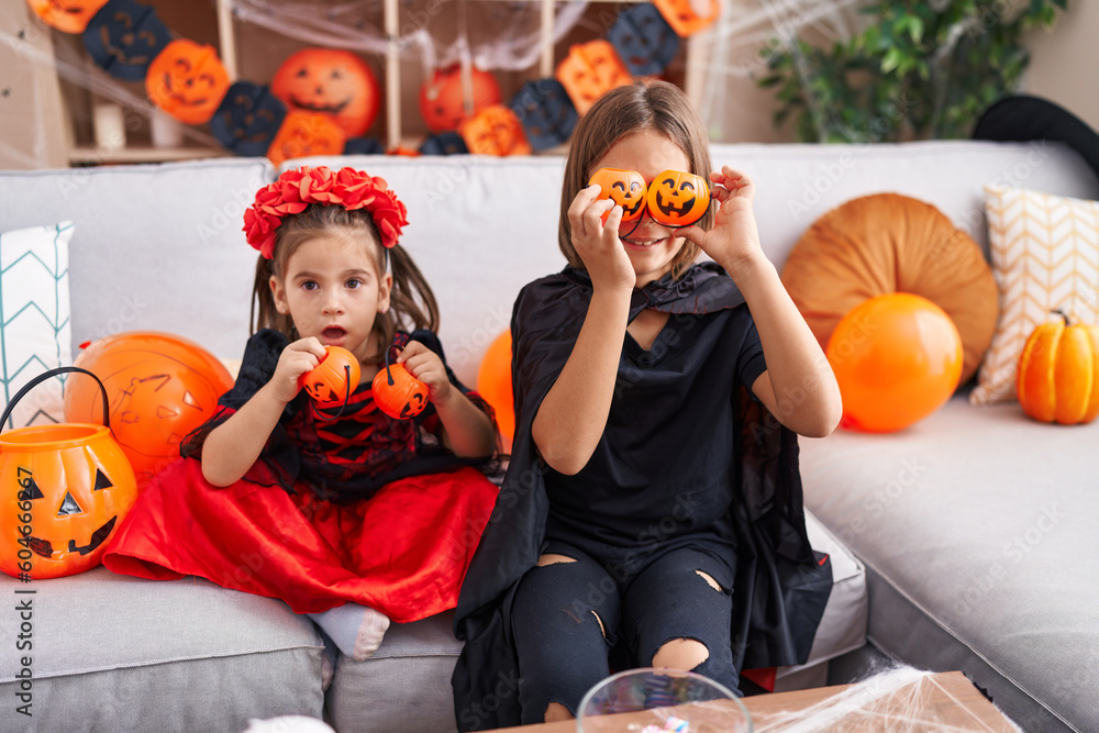 Adorable boy and girl wearing halloween costume holding pumpkin baskets over eyes at home
