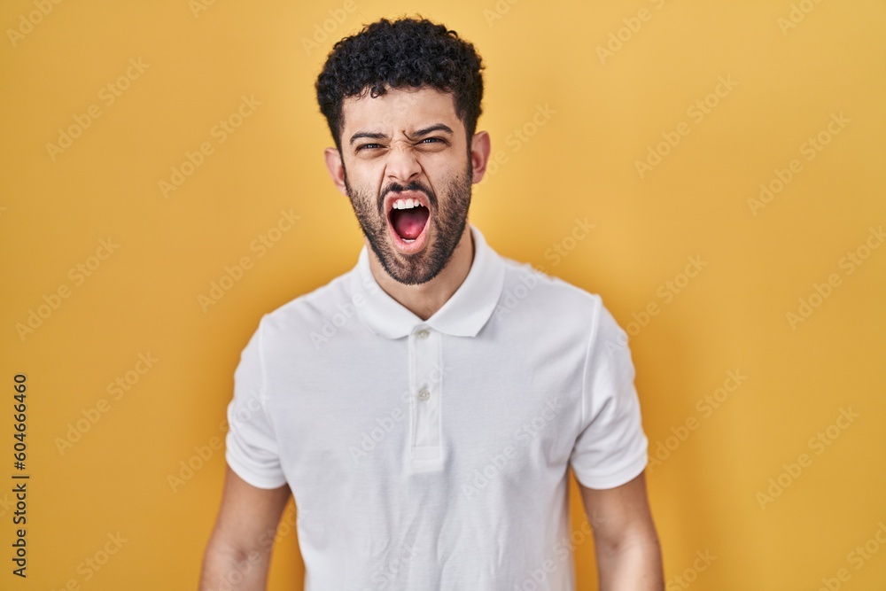 Arab man standing over yellow background angry and mad screaming frustrated and furious, shouting with anger. rage and aggressive concept. Arab man standing over yellow background angry and mad screaming frustrated and furious, shouting with anger. rage and aggressive concept.