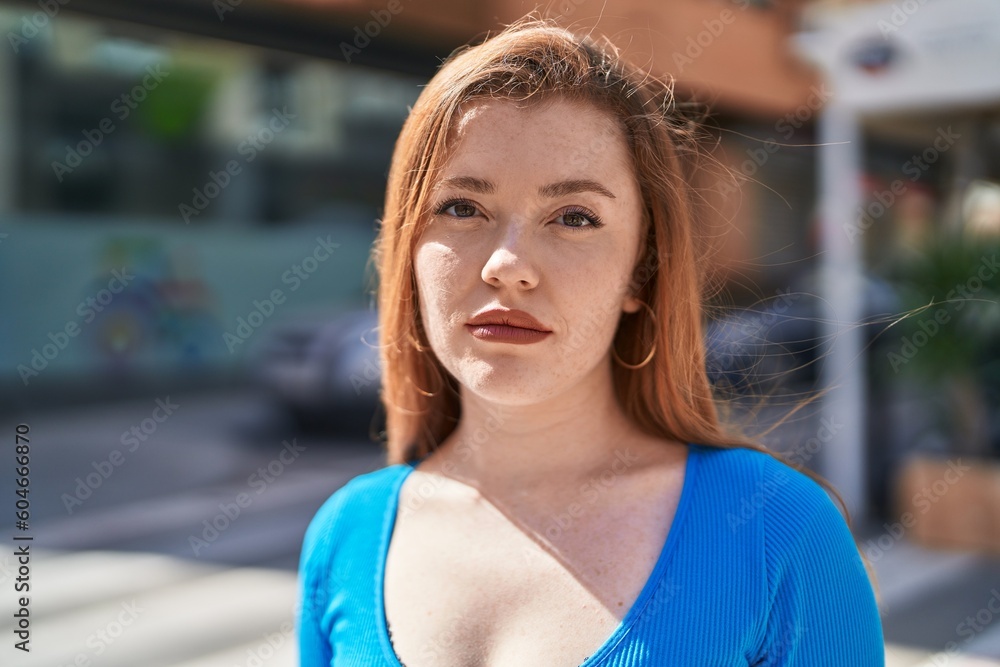 Young redhead woman standing with serious expression at street