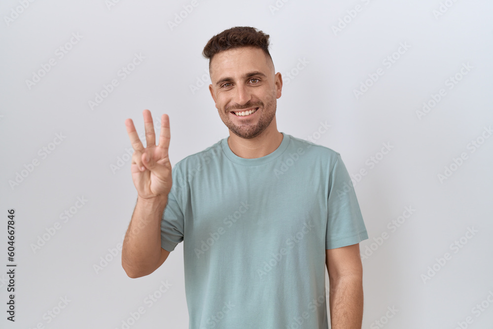 Fototapeta premium Hispanic man with beard standing over white background showing and pointing up with fingers number three while smiling confident and happy.