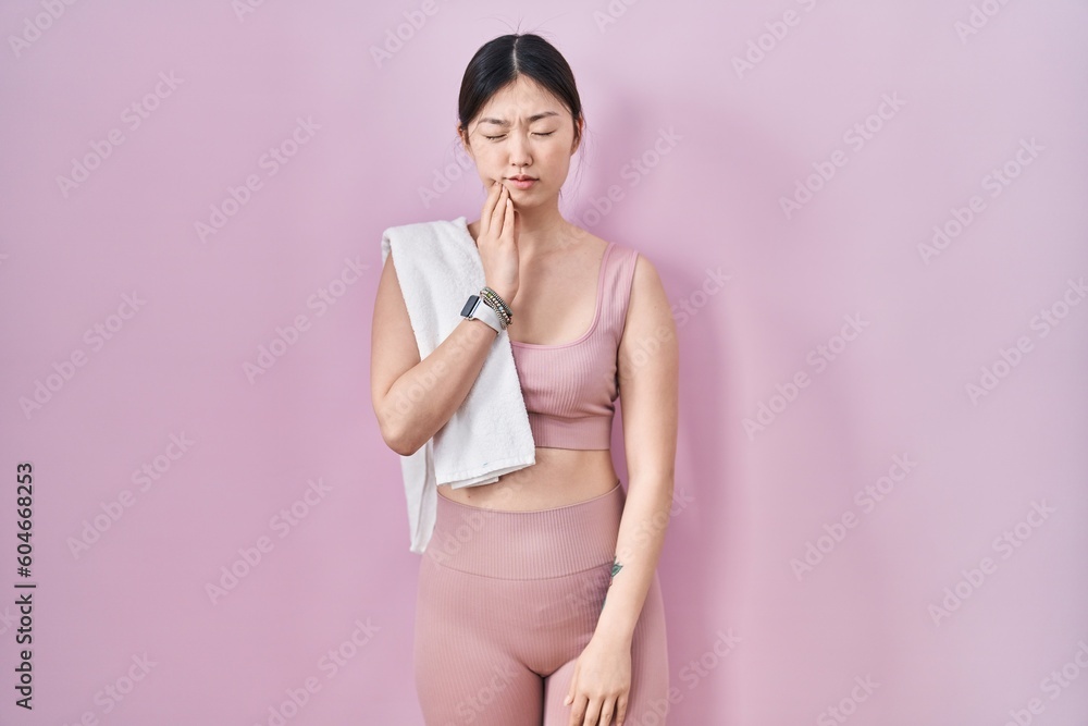 Chinese young woman wearing sportswear and towel touching mouth with hand with painful expression because of toothache or dental illness on teeth. dentist Chinese young woman wearing sportswear and towel touching mouth with hand with painful expression because of toothache or dental illness on teeth. dentist