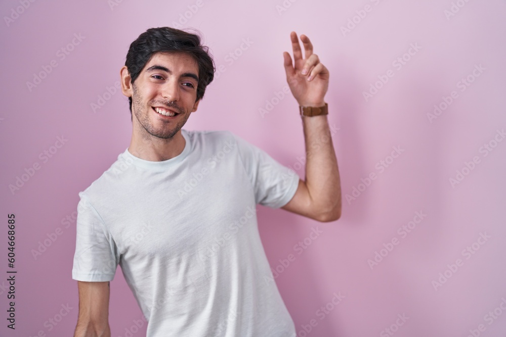 Young hispanic man standing over pink background dancing happy and cheerful, smiling moving casual and confident listening to music Young hispanic man standing over pink background dancing happy and cheerful, smiling moving casual and confident listening to music