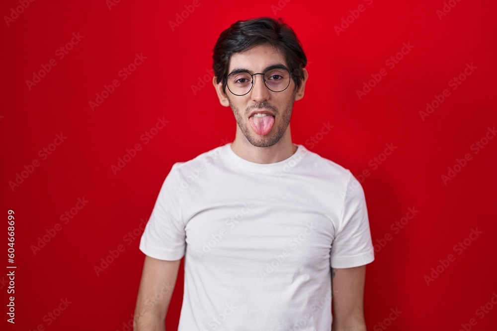 Young hispanic man standing over red background sticking tongue out happy with funny expression. emotion concept. Young hispanic man standing over red background sticking tongue out happy with funny expression. emotion concept.