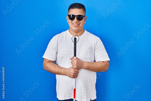 Hispanic young blind man holding cane smiling with a happy and cool smile on face. showing teeth. photo