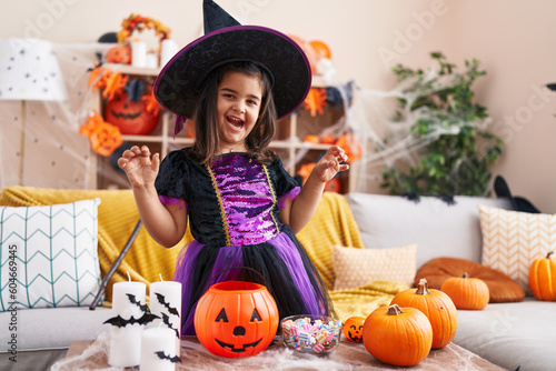 Adorable hispanic girl having halloween party doing scare gesture at home