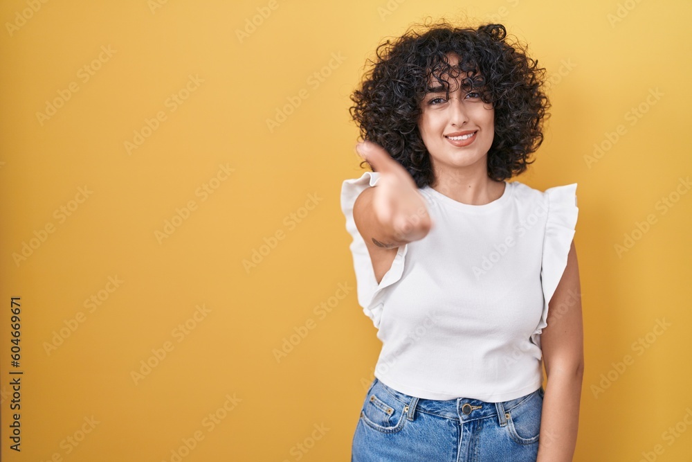 Young middle east woman standing over yellow background smiling friendly offering handshake as greeting and welcoming. successful business. Young middle east woman standing over yellow background smiling friendly offering handshake as greeting and welcoming. successful business.