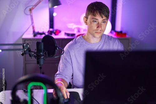 Young caucasian man streamer sitting on table with serious expression at gaming room © Krakenimages.com