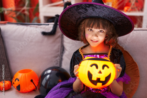Adorable hispanic girl having halloween party holding pumpkin lamp basket at home