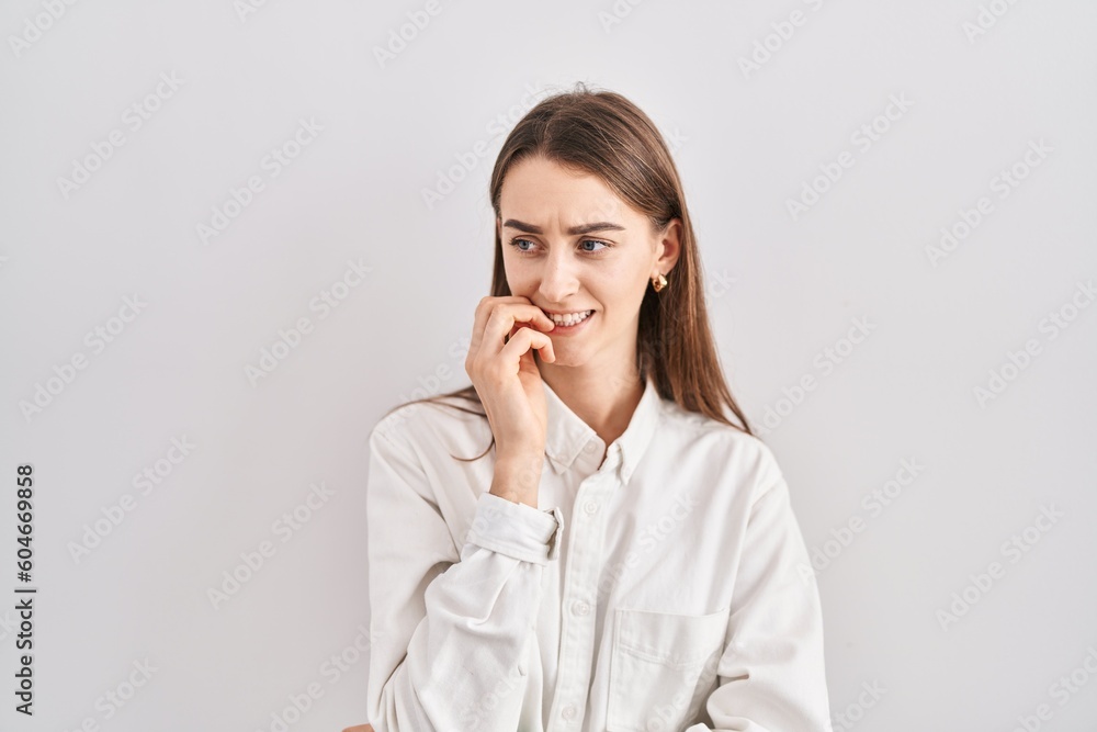 Young caucasian woman standing over isolated background looking stressed and nervous with hands on mouth biting nails. anxiety problem. Young caucasian woman standing over isolated background looking stressed and nervous with hands on mouth biting nails. anxiety problem.
