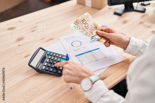 Young caucasian woman ecommerce business worker counting canada dollars using calculator at office