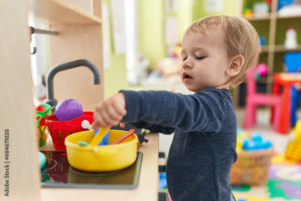 Adorable blond toddler playing with play kitchen standing at kindergarten Adorable blond toddler playing with play kitchen standing at kindergarten