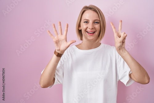 Young caucasian woman standing over pink background showing and pointing up with fingers number seven while smiling confident and happy.