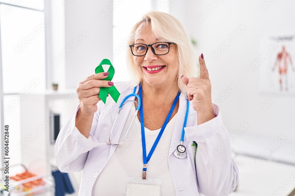Middle age caucasian woman holding support green ribbon surprised with an idea or question pointing finger with happy face, number one Middle age caucasian woman holding support green ribbon surprised with an idea or question pointing finger with happy face, number one