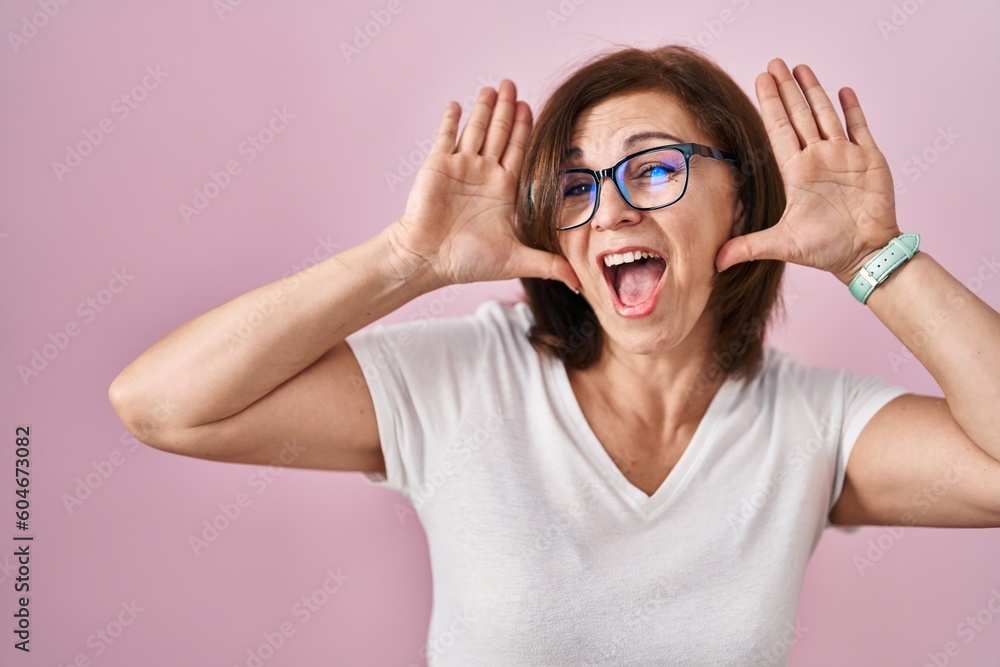 Middle age hispanic woman standing over pink background smiling cheerful playing peek a boo with hands showing face. surprised and exited Middle age hispanic woman standing over pink background smiling cheerful playing peek a boo with hands showing face. surprised and exited