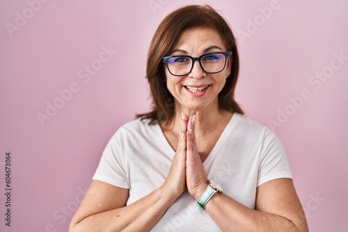 Fototapeta Naklejka Na Ścianę i Meble -  Middle age hispanic woman standing over pink background praying with hands together asking for forgiveness smiling confident.