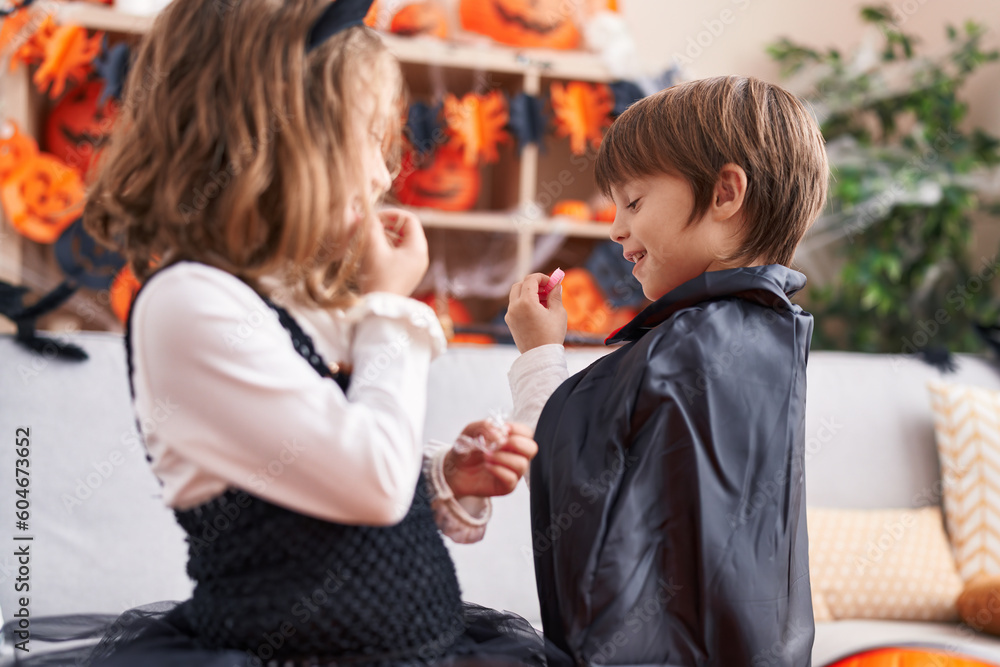 Adorable boy and girl having halloween party eating candies at home