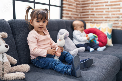 Adorable boy and girl sitting on sofa playing with dolls at home