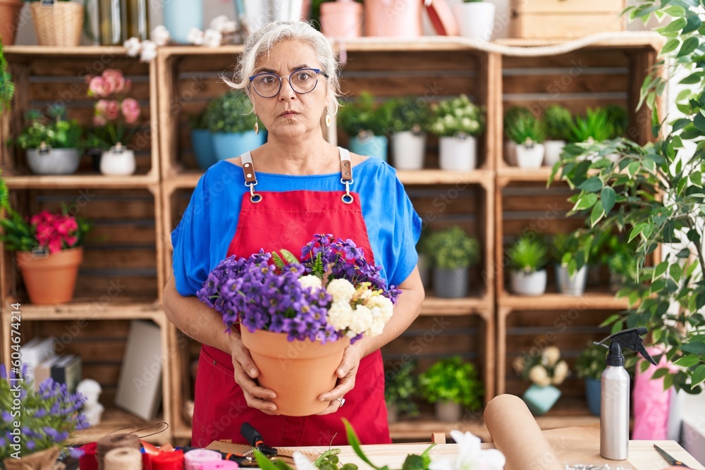 Middle age woman with grey hair working at florist shop holding plant skeptic and nervous, frowning upset because of problem. negative person.