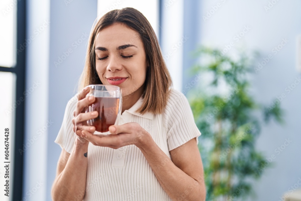 Young beautiful hispanic woman smiling confident smelling tea at home