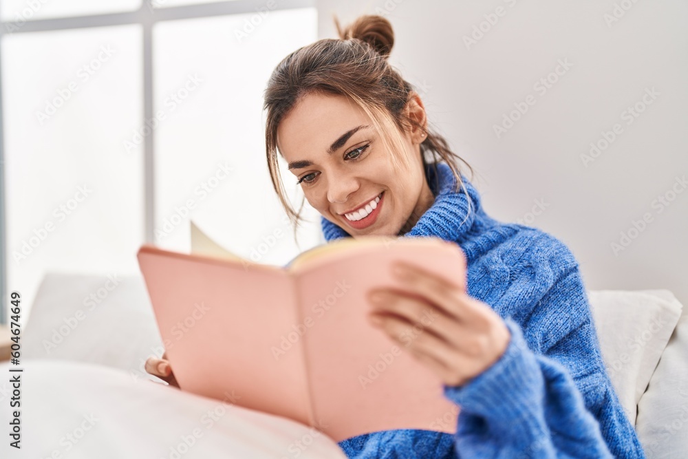 Young beautiful hispanic woman reading book sitting on bed at bedroom Young beautiful hispanic woman reading book sitting on bed at bedroom