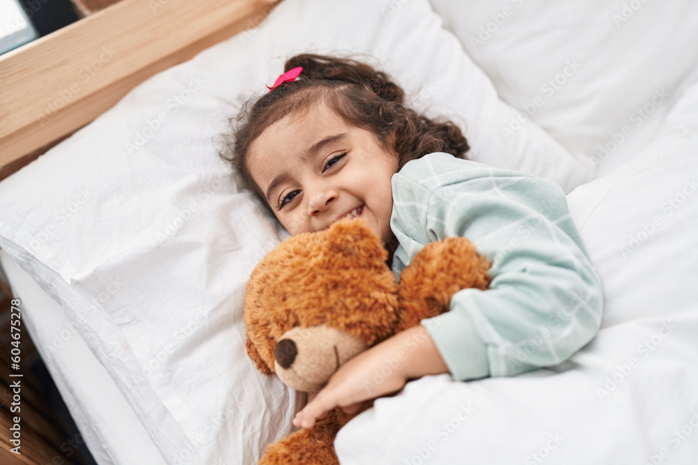 Adorable hispanic girl hugging teddy bear lying on bed at bedroom Adorable hispanic girl hugging teddy bear lying on bed at bedroom