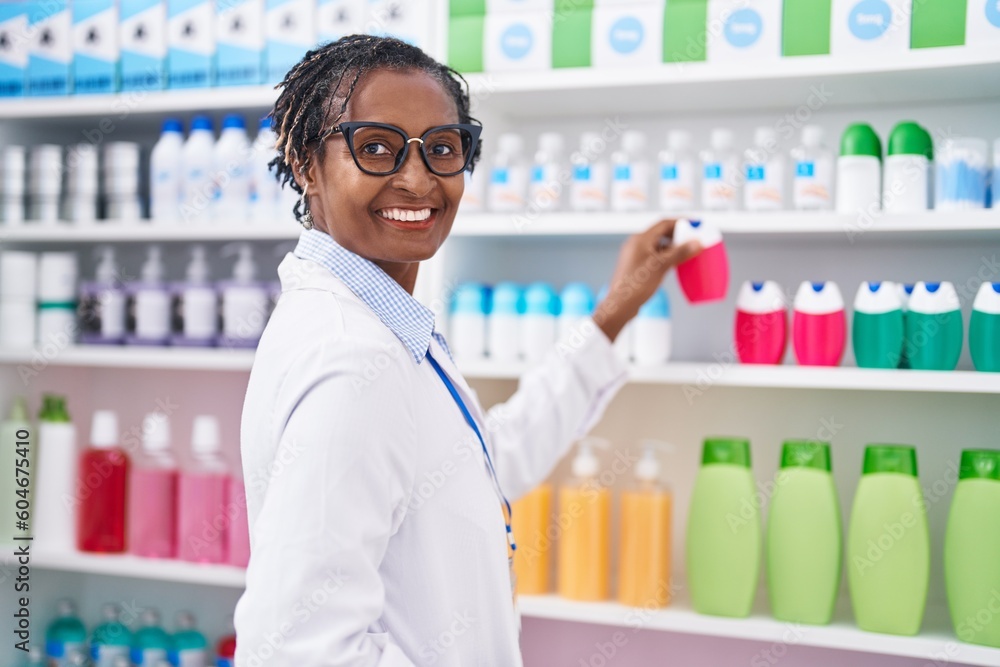 Middle age african american woman pharmacist smiling confident holding toothpaste on shelving at pharmacy