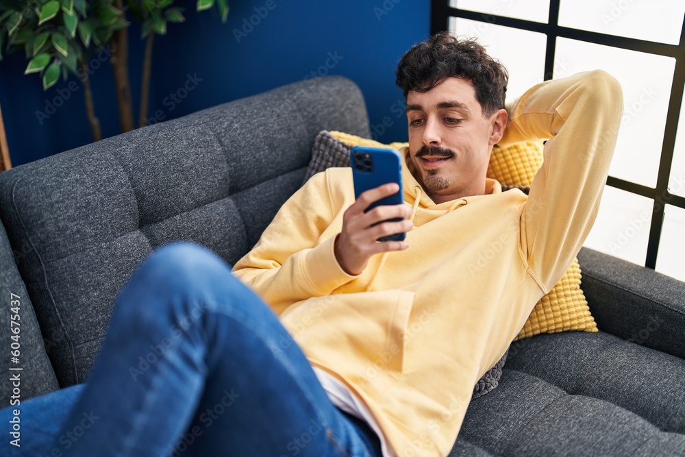 Young caucasian man using smartphone lying on sofa at home Young caucasian man using smartphone lying on sofa at home