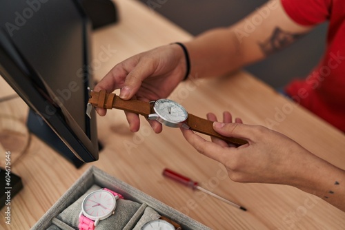 Young beautiful hispanic woman ecommerce business worker holding watch at office