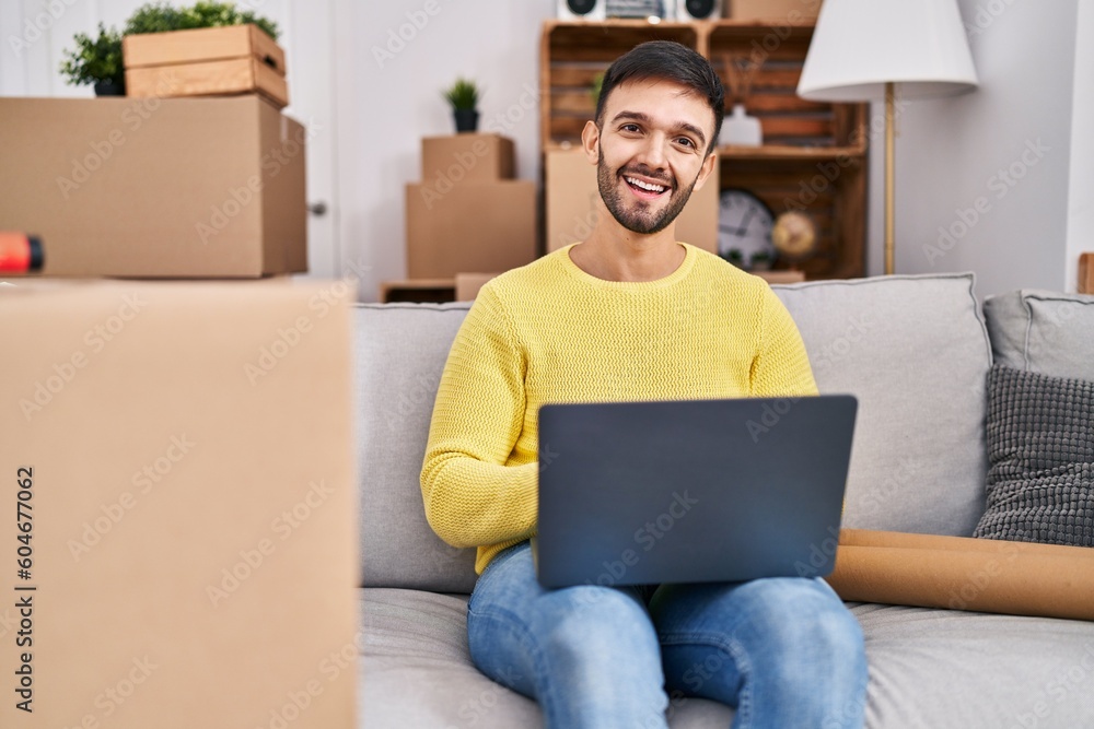 Young hispanic man using laptop sitting on sofa at new home Young hispanic man using laptop sitting on sofa at new home