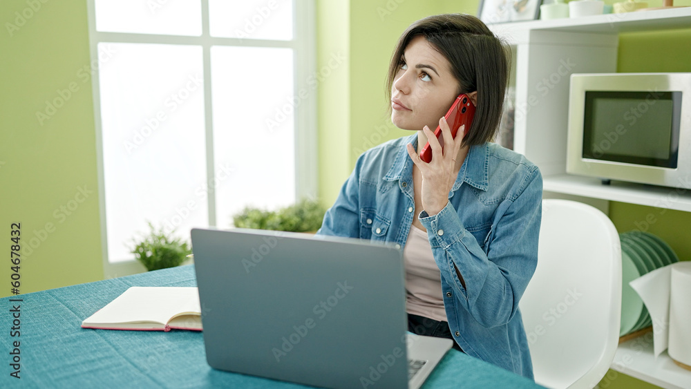 Young caucasian woman talking on smartphone using laptop at home Young caucasian woman talking on smartphone using laptop at home