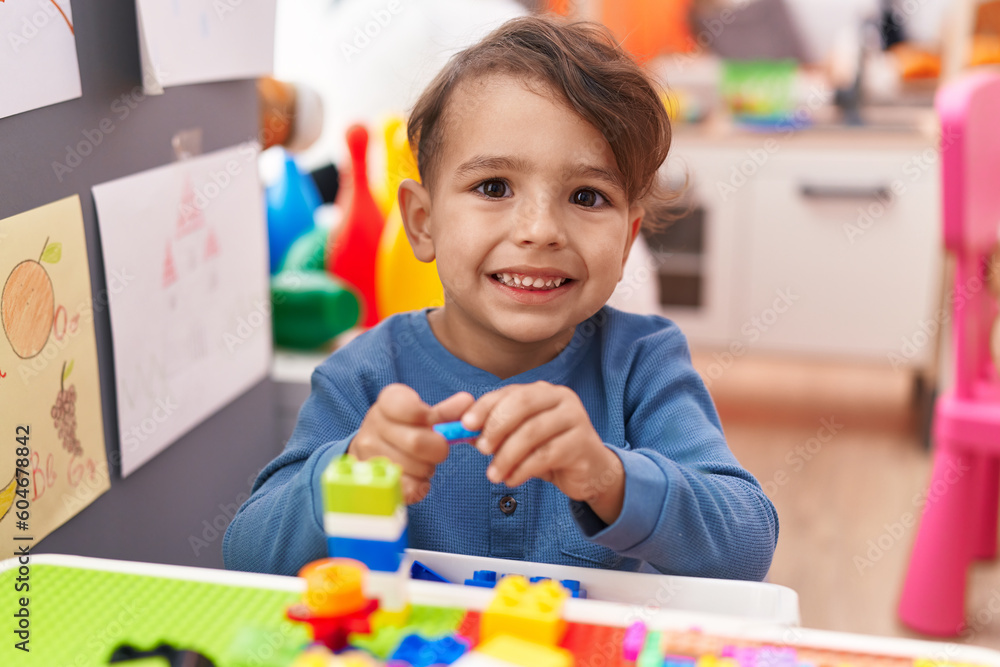 Fototapeta premium Adorable hispanic boy playing with construction blocks sitting on table at kindergarten