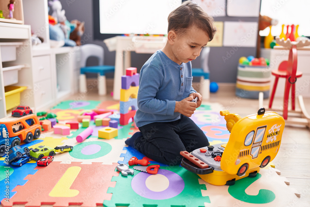 Adorable hispanic boy playing with tools toy sitting on floor at kindergarten Adorable hispanic boy playing with tools toy sitting on floor at kindergarten