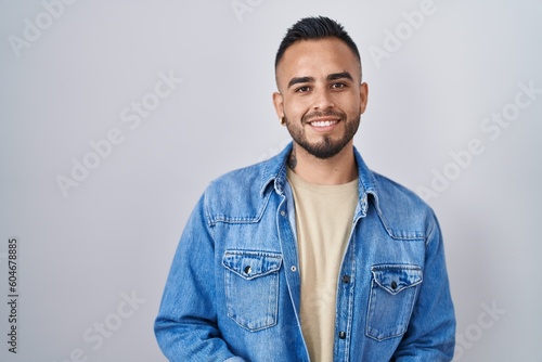 Young hispanic man standing over isolated background with hands together and crossed fingers smiling relaxed and cheerful. success and optimistic
