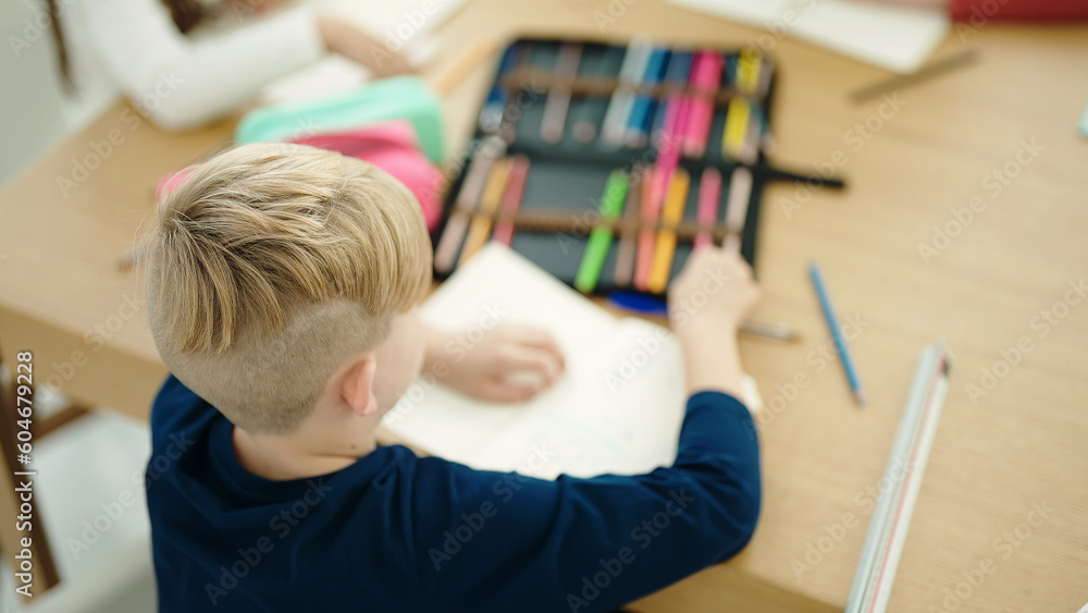 Adorable caucasian boy student drawing on notebook sitting on table at classroom Adorable caucasian boy student drawing on notebook sitting on table at classroom