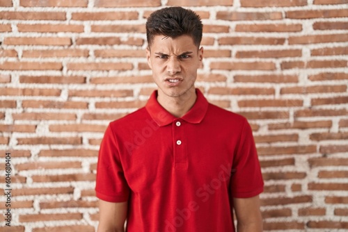 Young hispanic man standing over bricks wall skeptic and nervous, frowning upset because of problem. negative person.