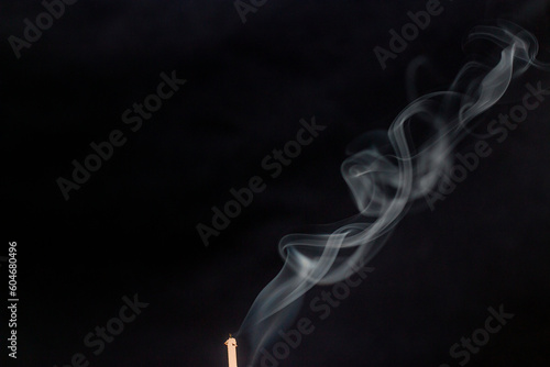 White smoke from incense wraps beautifully in the air on a dark background close-up