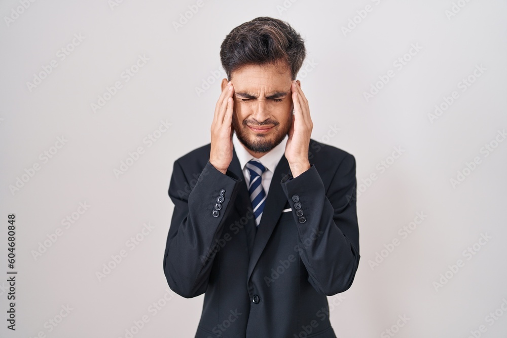Young hispanic man with tattoos wearing business suit and tie with hand on head, headache because stress. suffering migraine. Young hispanic man with tattoos wearing business suit and tie with hand on head, headache because stress. suffering migraine.