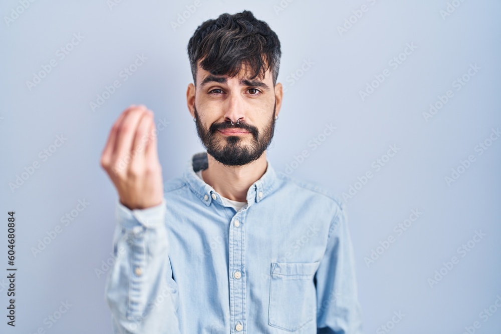 Young hispanic man with beard standing over blue background doing italian gesture with hand and fingers confident expression Young hispanic man with beard standing over blue background doing italian gesture with hand and fingers confident expression