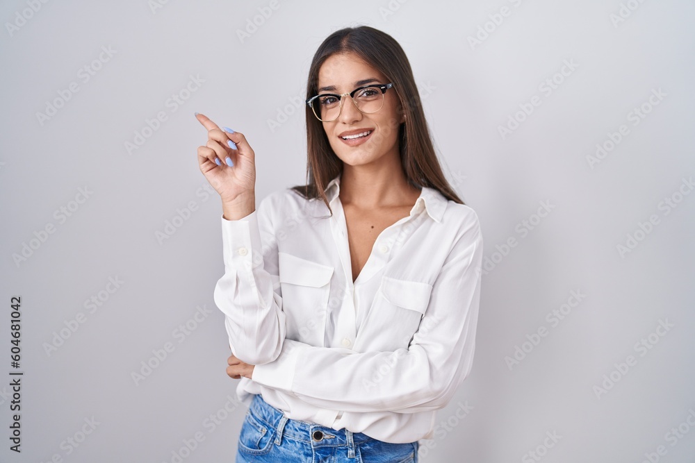 Young brunette woman wearing glasses with a big smile on face, pointing with hand finger to the side looking at the camera. Young brunette woman wearing glasses with a big smile on face, pointing with hand finger to the side looking at the camera.