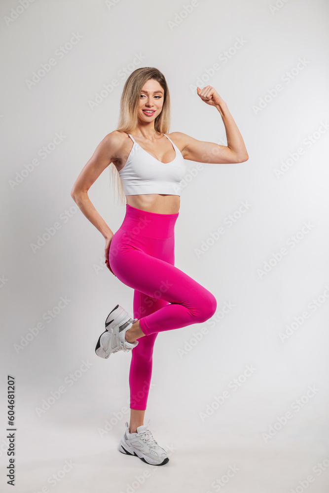 Beautiful young athletic fit woman with a slender body in fashionable sportswear with a top, pink leggings and sneakers on a white background
