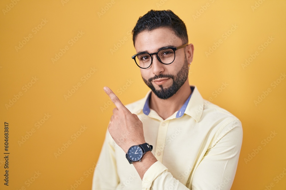 Hispanic young man wearing business clothes and glasses pointing with hand finger to the side showing advertisement, serious and calm face Hispanic young man wearing business clothes and glasses pointing with hand finger to the side showing advertisement, serious and calm face